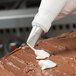 A hand using an Ateco 103 rose piping tip in a pastry bag to frost a cake.