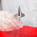 A hand in a glove holding an Ateco stainless steel flower nail with a spike on the top.
