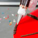 A person using an Ateco plain piping tip to decorate a red cake with chocolate frosting.