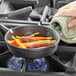 A hand using a green cloth to hold a Valor mini cast iron skillet filled with cooked carrots.