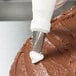 A person using an Ateco pastry bag with a rose tip to decorate a cake.