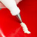 A hand using an Ateco curved petal piping tip to pipe white frosting on a tooth.
