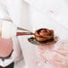 A person using an Ateco flower nail to pipe chocolate frosting on a cake.