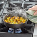 A hand holding a Valor pre-seasoned cast iron mini skillet of food on a stove.