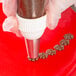 A hand using an Ateco grass piping tip in a pastry bag to decorate a cake with chocolate.
