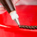 A person's hand using an Ateco plain piping tip on a red cake.