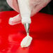 A hand holding a pastry bag with white frosting using an Ateco ruffle piping tip.