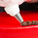 A person using an Ateco drop flower piping tip on a pastry bag to decorate a cake.