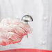 A gloved hand holding an Ateco stainless steel domed flower nail.