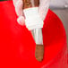 A hand using an Ateco Rose Leaf piping tip in a pastry bag to decorate a red cake.