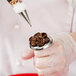 A person holding a pastry bag with a brown flower on a ring using an Ateco stainless steel flower nail.