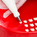 A hand using an Ateco curved petal piping tip to decorate a red cake.