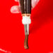 A hand holding a metal Ateco notched ruffle piping tip over a tube of brown liquid.