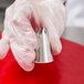 A hand in a glove holding a silver Ateco Swirl Top Piping Tip.