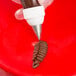 A hand holding a pastry bag with a rose leaf piping tip over a red bowl.