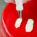 A person using an Ateco leaf piping tip to put cream on a red surface.