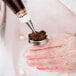 A person using an Ateco stainless steel flower nail to pipe chocolate frosting on a pastry.