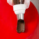 A hand using an Ateco U-shape ruffle piping tip to pipe chocolate frosting onto a cake.