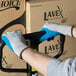 A man wearing Cordova gray gloves with blue latex palm coating holding a box.