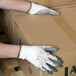 A person wearing Cordova white polyester gloves with gray nitrile palm coating on a box.