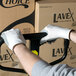 A man wearing Cordova white gloves with gray palms holding a box on a hand truck.