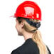 A woman wearing a Cordova red cap style hard hat with a ponytail.