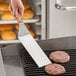 A person cooking burgers on a grill with an American Metalcraft solid turner with a wood handle.