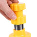 A hand holding a yellow and silver Weston corn stripper over a yellow plastic container.
