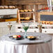 A Tablecraft round aluminum table cover with random swirl design on a round table set with food and wine.