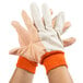 A pair of hands wearing large orange and white Cordova cotton canvas work gloves with PVC dots.