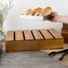 A Tablecraft acacia wood crate holding a tray of bread on a table.