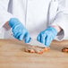 A person in blue gloves using a Choice chef knife to cut meat.