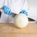 A person in blue gloves using a Choice chef knife to cut a melon.