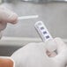 A person in white gloves using an FMP chlorine sanitizer test strip to test liquid in a vial.