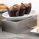 A Tablecraft stainless steel rectangular bowl filled with muffins on a table.