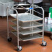 A man using a Vollrath stainless steel mobile mixing bowl stand with tray slides.