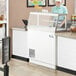 A woman in a white hat working at a refrigerated Avantco ice cream dipping cabinet.