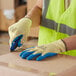 A person wearing Cordova yellow and blue gloves and a safety vest using a cutter to cut a box.