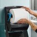 A large white hardwound paper towel roll being loaded into a black wall-mounted dispenser.