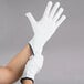 A person wearing Cordova white nylon work gloves on their hand.