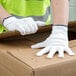 A person wearing Cordova white nylon work gloves holding a cardboard box.