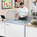 A man in a white shirt and black pants standing at a counter with a glass top over ice cream.