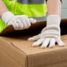 A person wearing Cordova lightweight natural polyester/cotton work gloves opening a cardboard box.