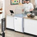 A man in a white uniform and cap using an Avantco ice cream dipping cabinet.