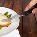 A person using a Walco steak knife to cut meat on a plate.