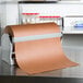 A Bulman deluxe all-in-one paper dispenser/cutter holding a roll of brown paper on a metal counter.