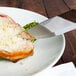 A Walco steak knife with a jumbo Brazil Polywood handle cutting a piece of meat on a plate.