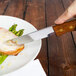 A Walco Utica II steak knife cutting meat on a plate.