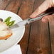 A person using a Walco Erie stainless steel steak knife to cut meat on a plate with asparagus.