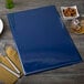 A dark blue Menu Solutions menu board on a table with a fork and knife.